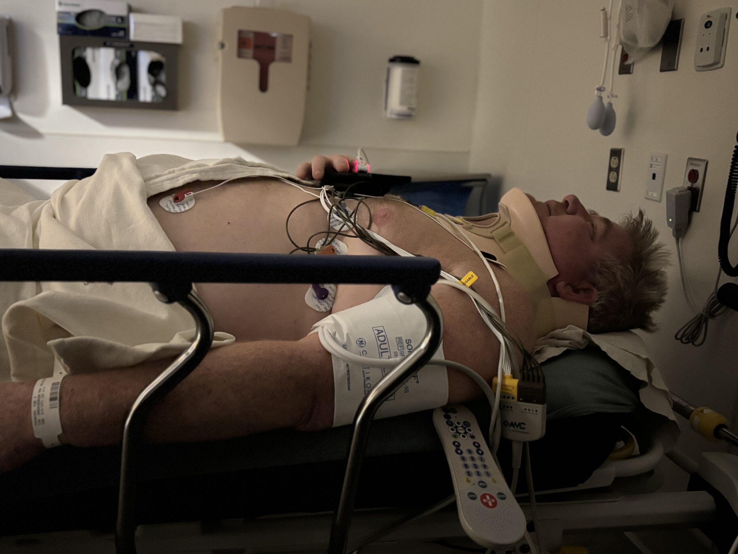 Rick in a hospital bed wearing a cervical collar, connected to monitors during his spinal injury recovery